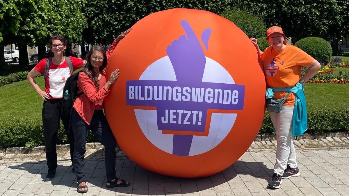 Drei Frauen stehen an einem orangenen Ball, auf dem "Bildungswende Jetzt!" steht.