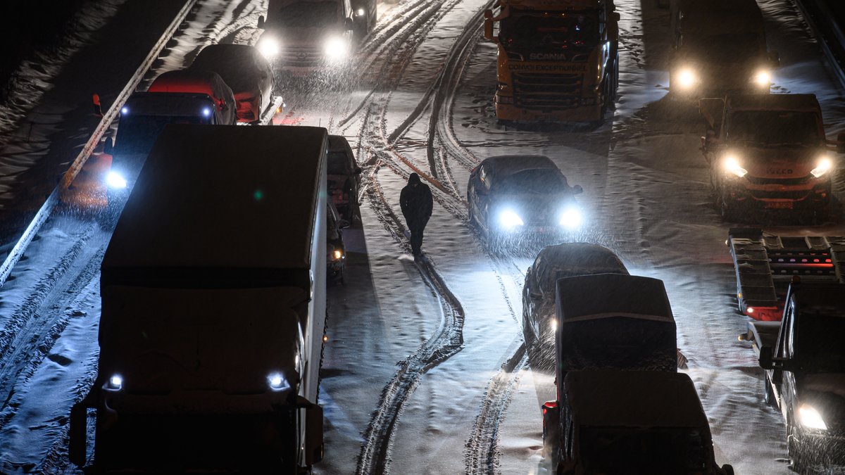 Autos und Lastwagen stehen am frühen Morgen bei Schneefall auf der verschneiten Autobahn 4 bei Dresden im Stau.