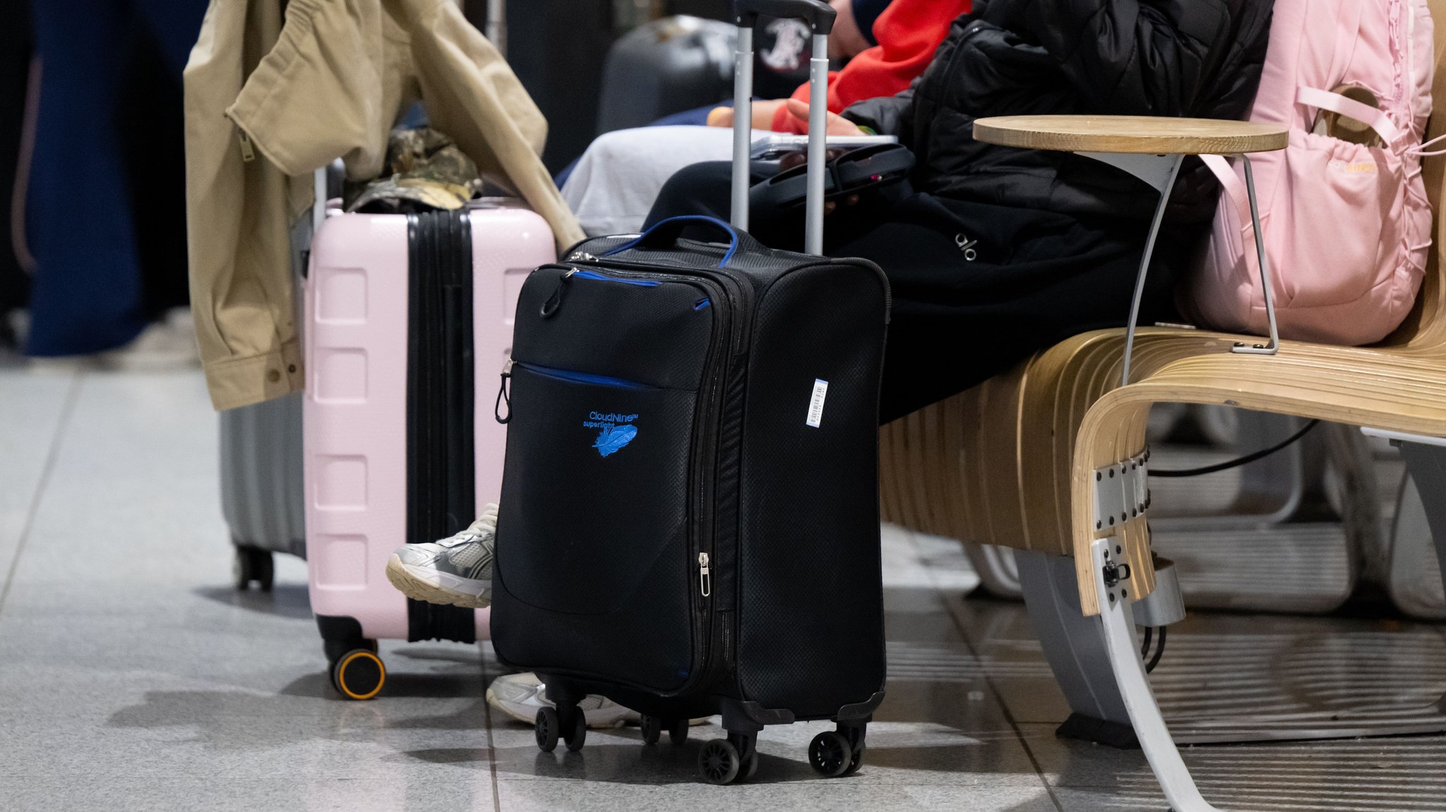  Passagiere stehen am Münchner Flughafen mit ihrem Gepäck an einem Check-In Schalter. 