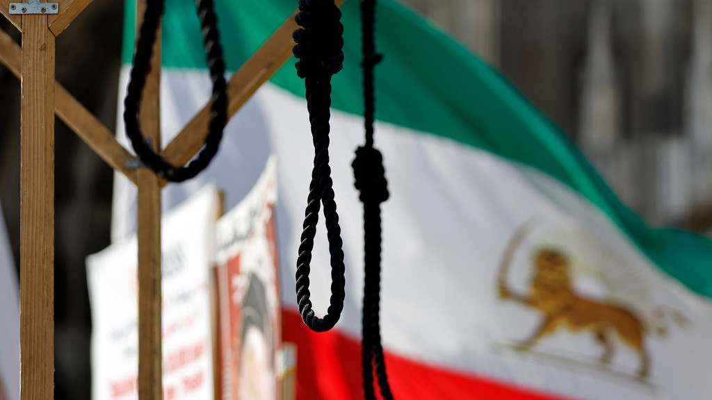 Stricke vor einer iranischen Flagge (Archivbild von einer Demonstration)