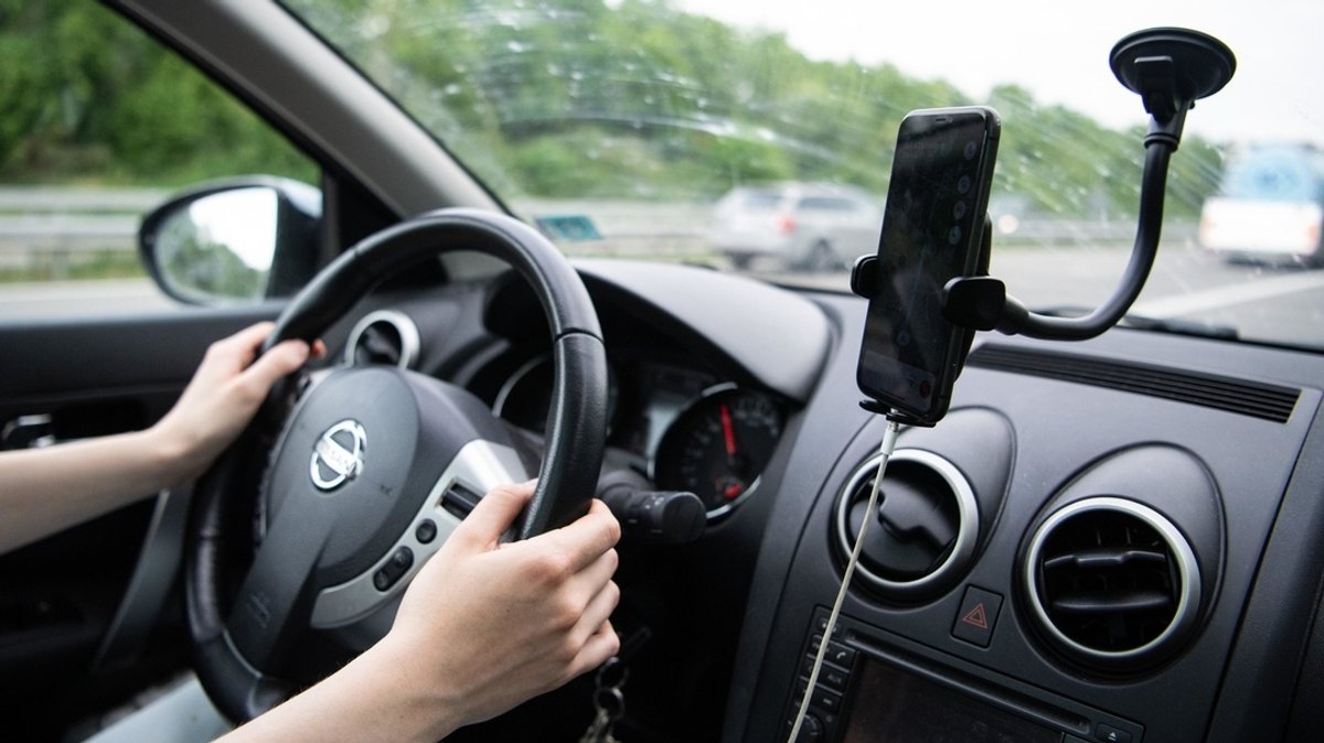 Eine Frau sitzt im Auto mit einem Smartphone in einer Halterung.