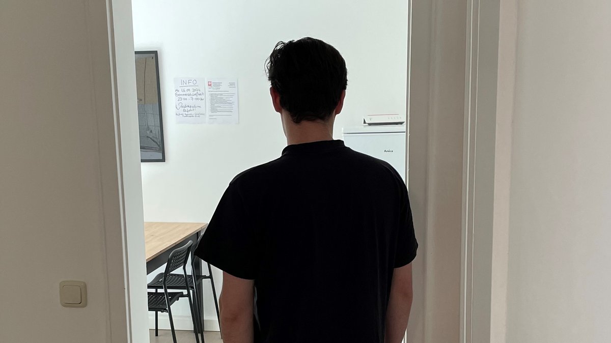 Ein junger Erwachsener in schwarzem T-Shirt steht in der Tür zu einem Zimmer in der Notschlafstelle für junge Erwachsene in Augsburg