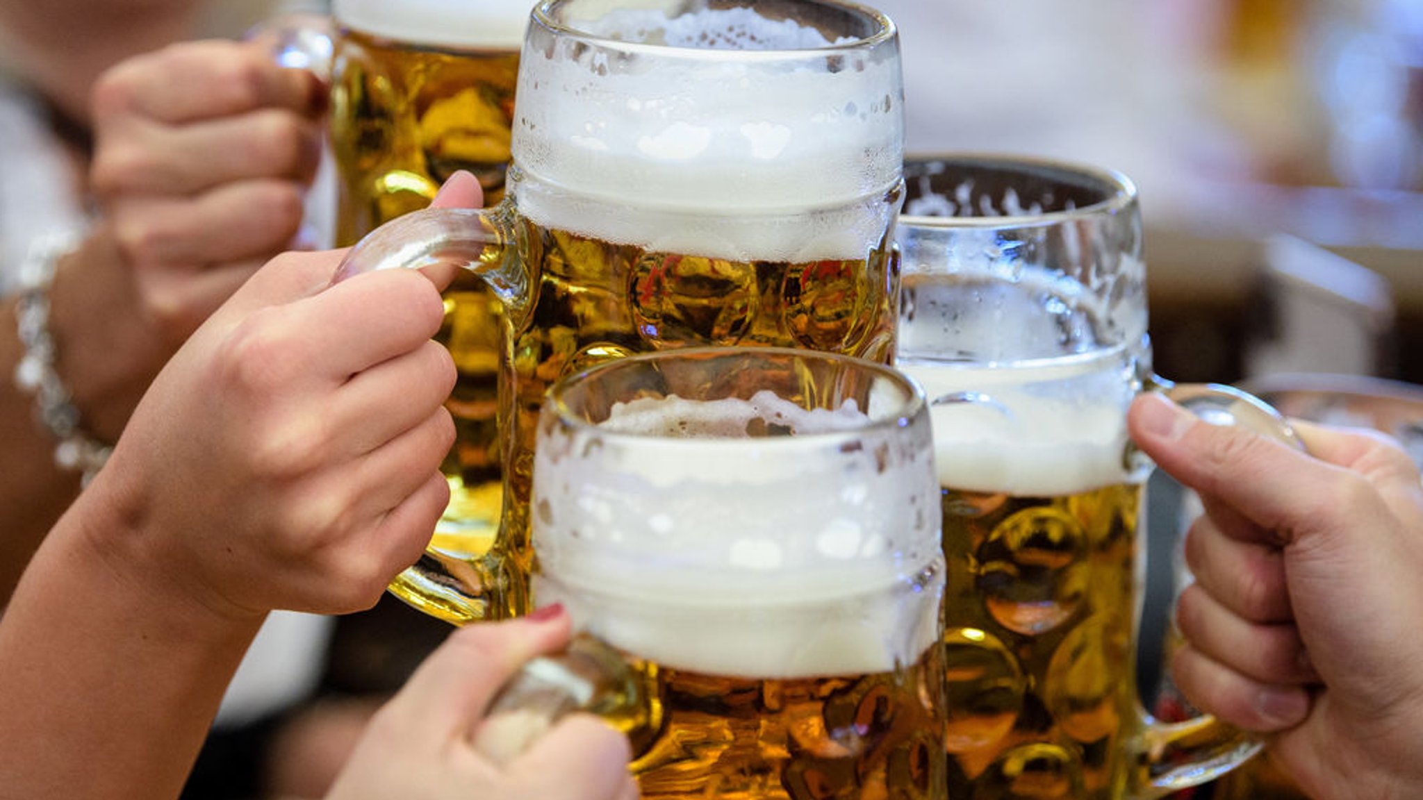 Besucherinnen prosten sich mit Bier in Maßkrügen zu.