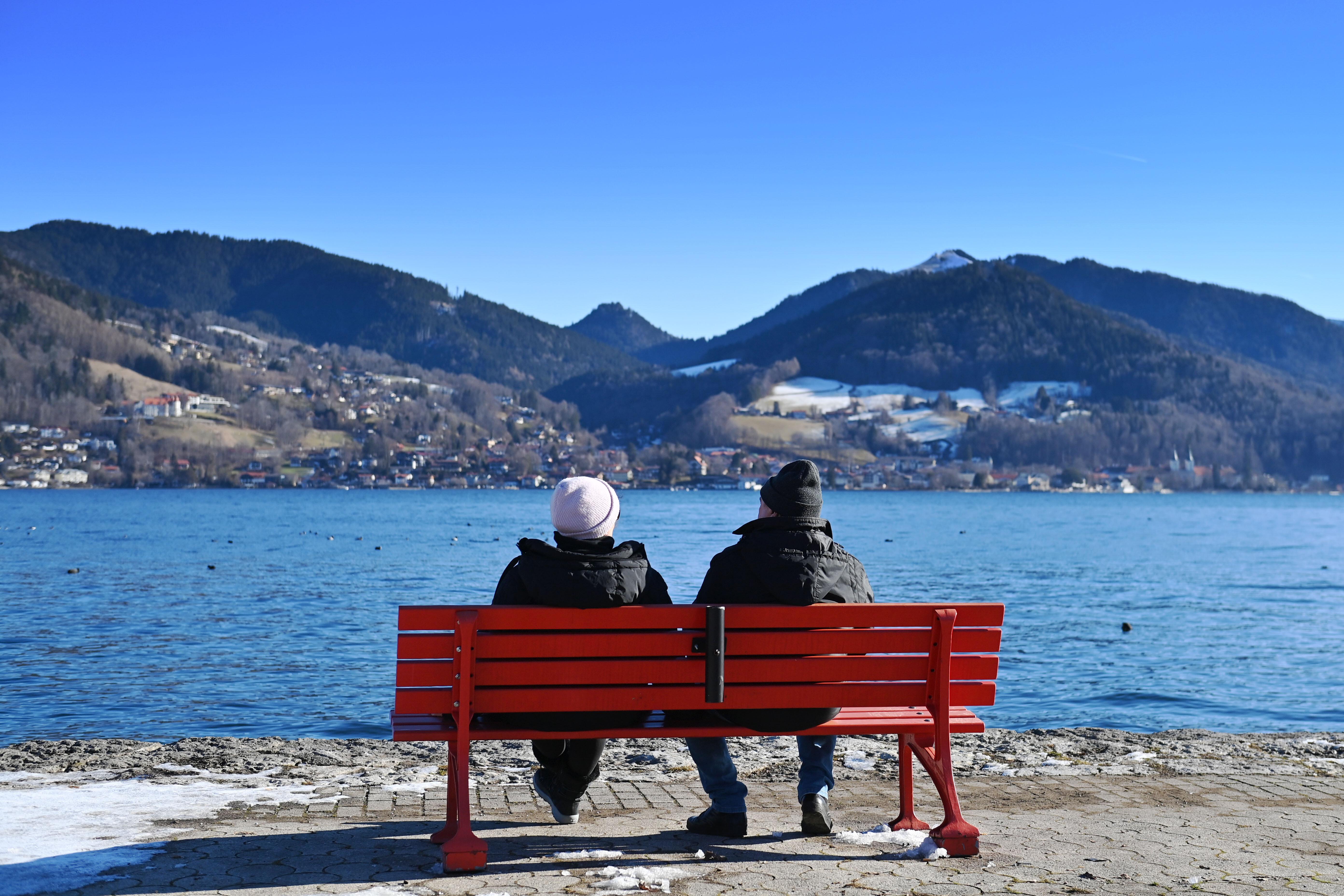 Strahlend blauer Himmel am Ufer vom Tegernsee in Bad Wiessee, ein Rentnerehepaar sitzt auf einer Bank.