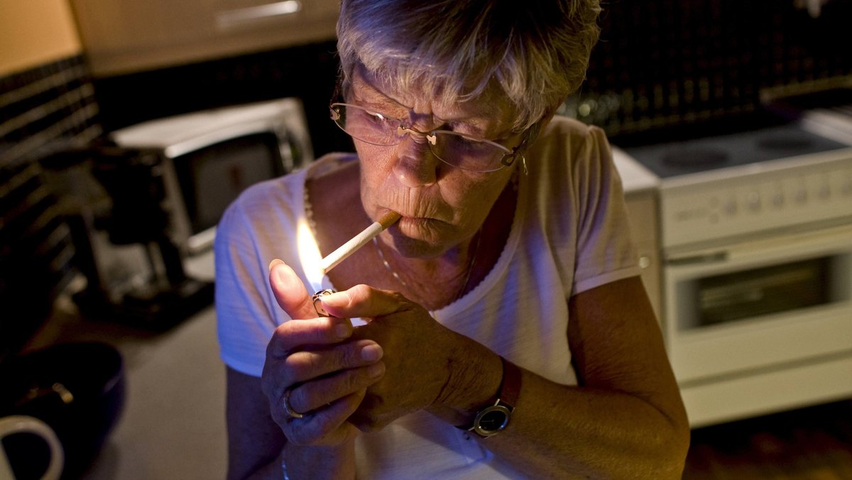 Ältere Frau raucht in der Küche