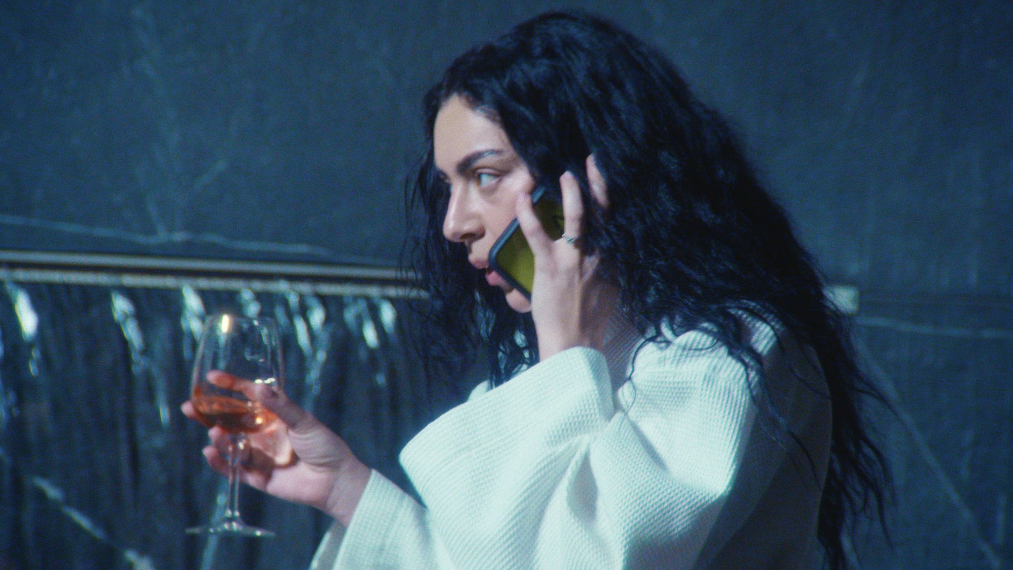 Charli xcx mit Handy und Weinglas in der Hand