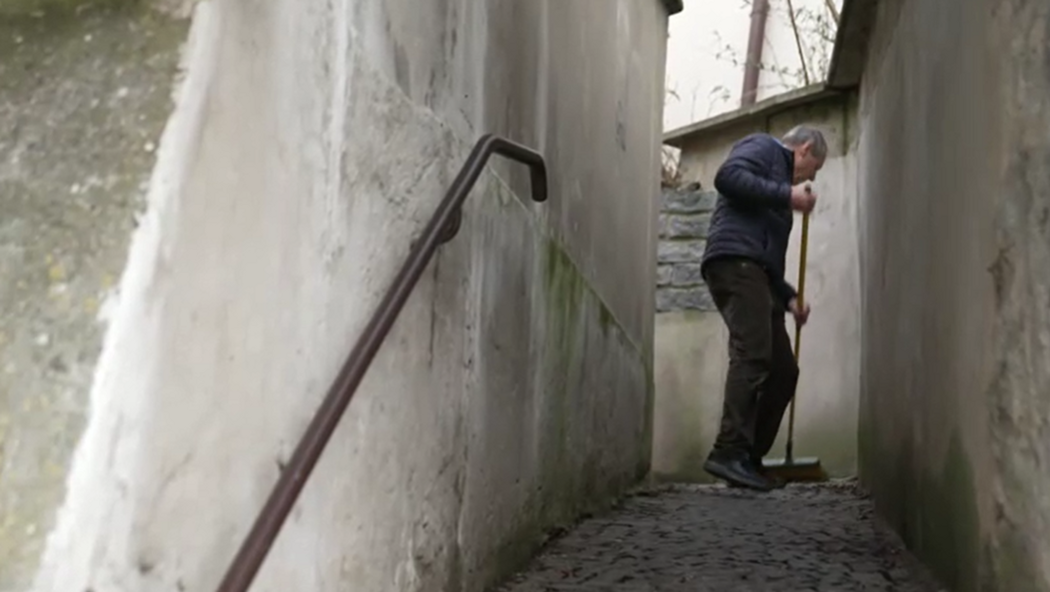 Ein Mann kehrt in der Passauer Altstadt den Gehweg vor seinem Haus.