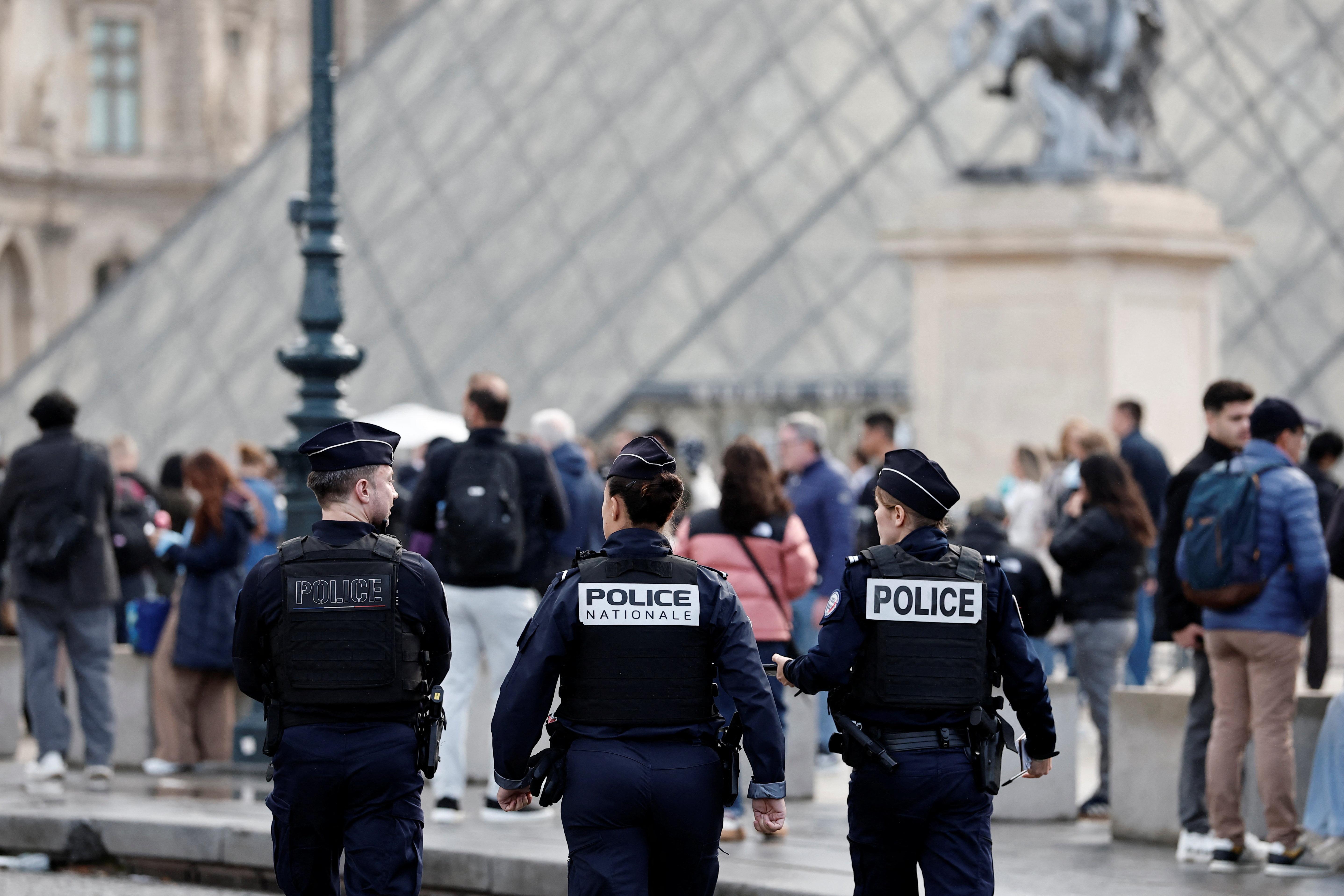 Zwei Polizistinnen und ein Polizist stehen vor der Glaspyramide des Louvre.