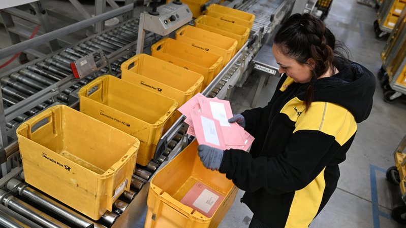 13.01.2025, Hessen, Mainz-Kastel: Briefwahl-Dummys werden in einem Briefzentrum der Deutschen Post bei einem Testlauf von Teamleiterin Romina Viniguerra kontrolliert. Die Post hat die automatische Sortierung und Versendung von Wahlbriefumschlägen für die Bundestagswahl in Hessen längst getestet. | Bild: dpa-Bildfunk/Arne Dedert 13.01.2025, Hessen, Mainz-Kastel: Briefwahl-Dummys werden in einem Briefzentrum der Deutschen Post bei einem Testlauf von Teamleiterin Romina Viniguerra kontrolliert. Die Post hat die automatische Sortierung und Versendung von Wahlbriefumschlägen für die Bundestagswahl in Hessen längst getestet.