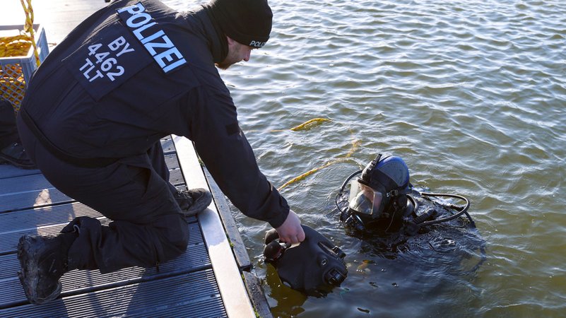 Ein Polizist übergibt einem Taucher ein Sonargerät. | Bild: dpa-Bildfunk/Heiko Becker Ein Polizist übergibt einem Taucher ein Sonargerät.