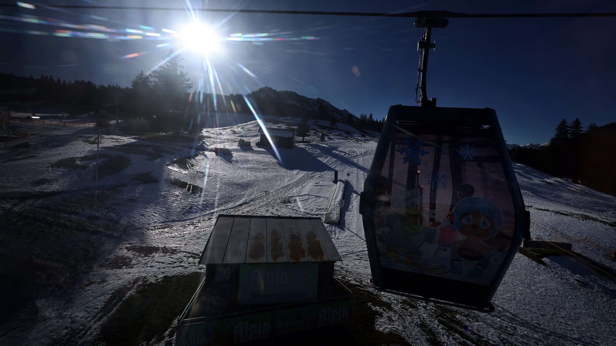 Eine Gondel der Söllereckbahn fährt nahe der Talstation im Sonnenschein über die teilweise mit Schnee bedeckte Landschaft (Archiv).