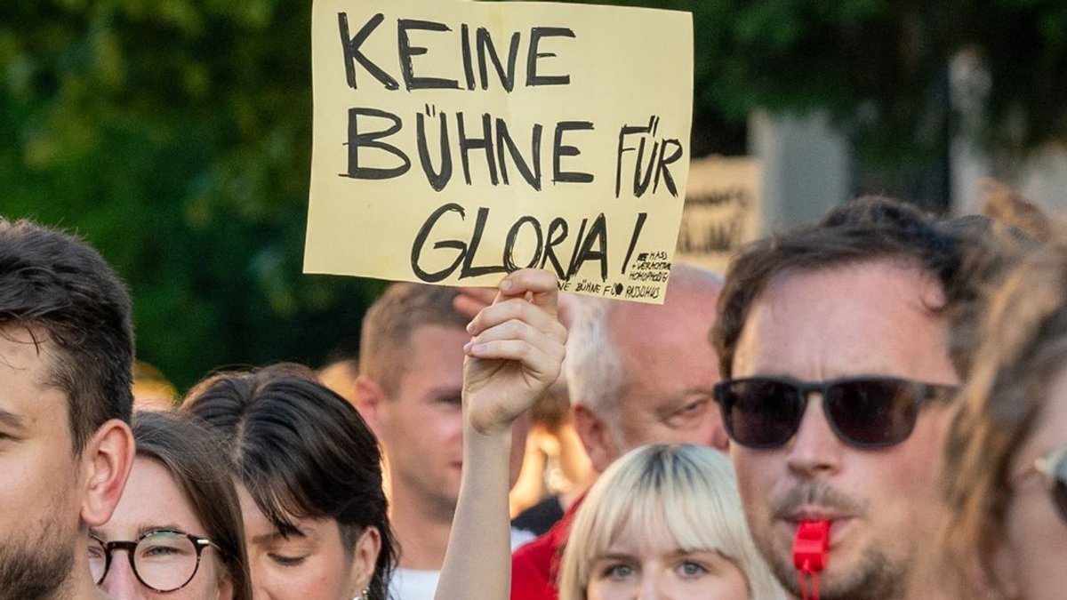 Ein Schild mit der Aufschrift "Keine Bühne für Gloria!" wird während einer Demonstration vor dem Fürstenschloss St. Emmeram in die Höhe gehalten. 