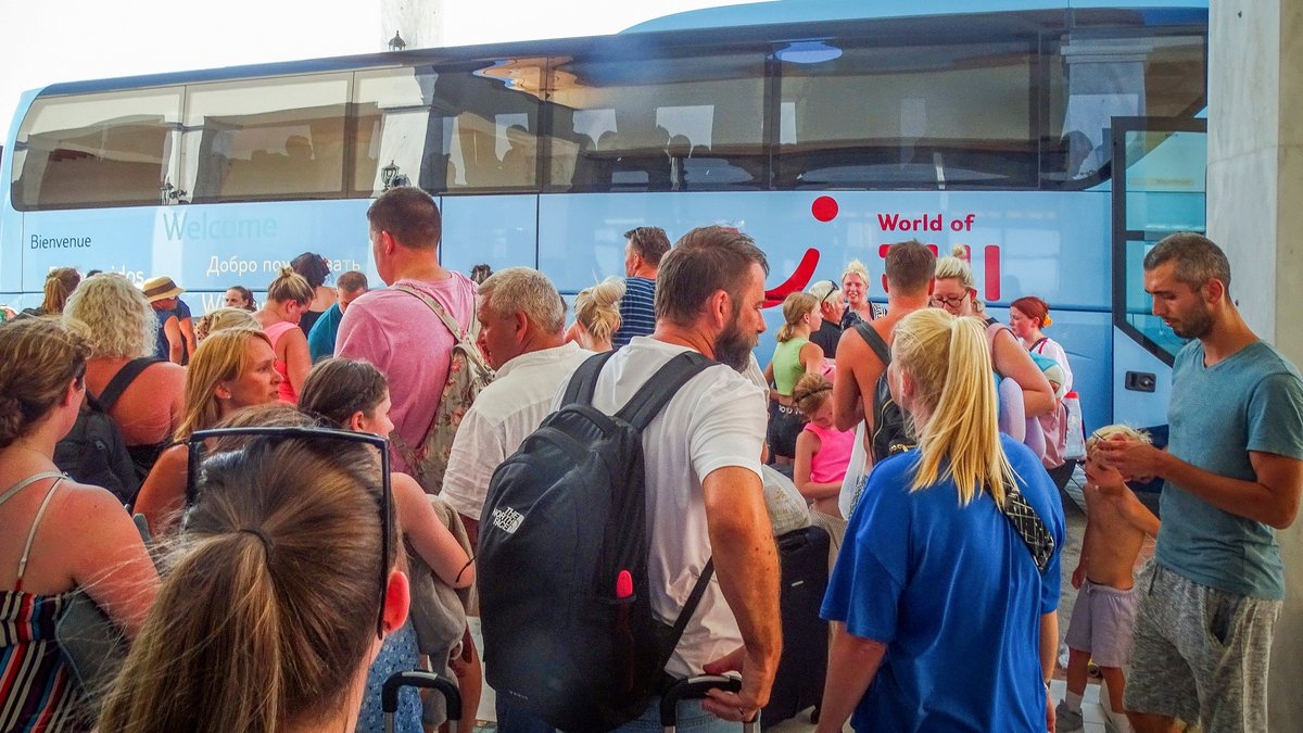 Touristen warten vor ihrem Hotel auf der griechischen Insel Rhodos auf den Einstieg in einen Bus, um die Insel Rhodos zu verlassen. 