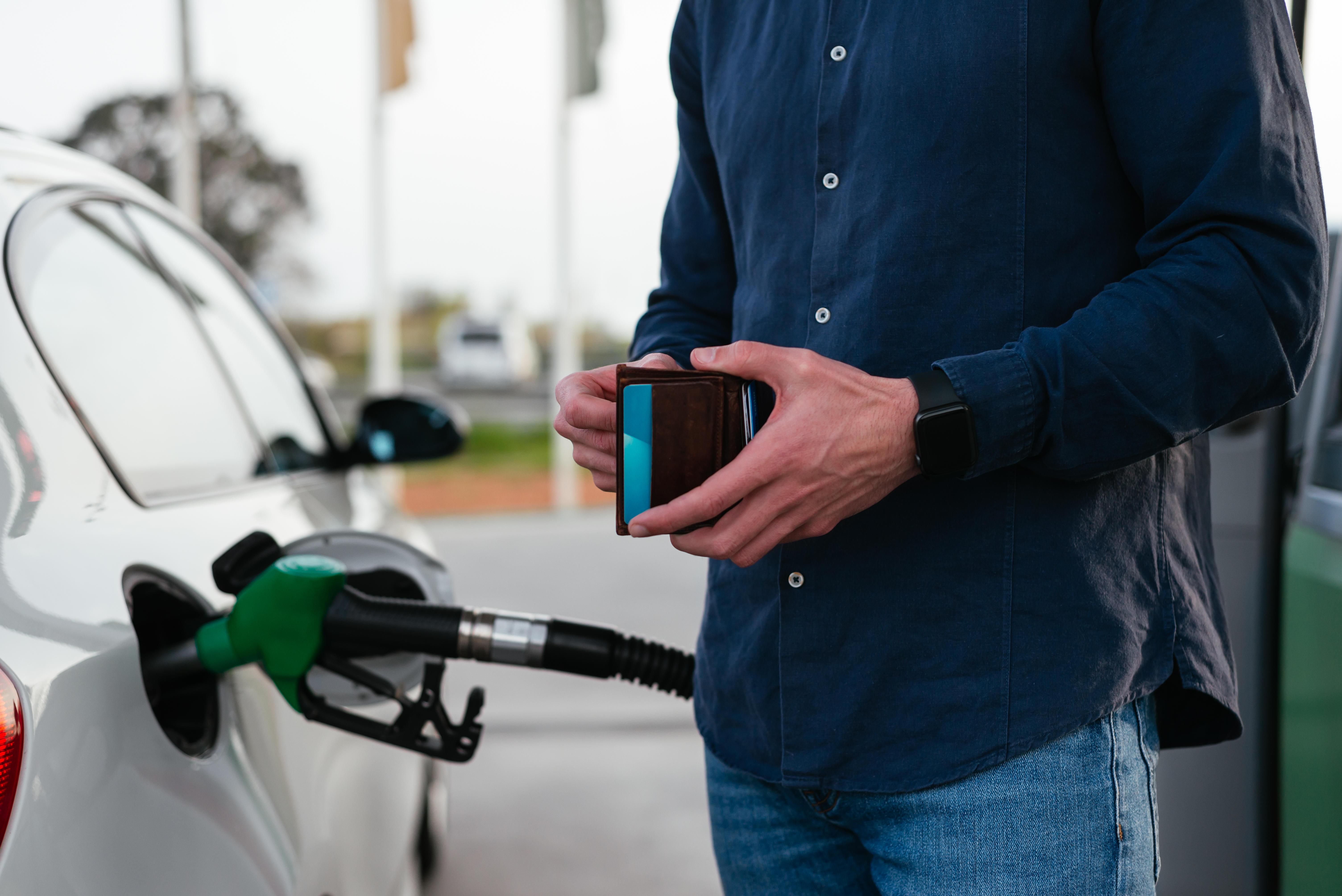 (Symbolbild) Ein Mann steht an einer Tankstelle und schaut in seinen Geldbeutel.