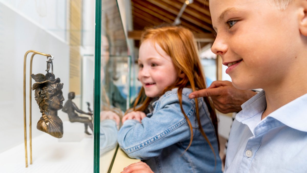 Zwei Kinder betrachten den Merkurkopf in der neuen Dauerausstellung. Er diente den Römern als Gewicht.