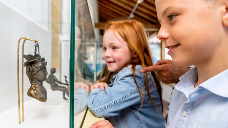 Zwei Kinder betrachten den Merkurkopf in der neuen Dauerausstellung. Er diente den Römern als Gewicht.