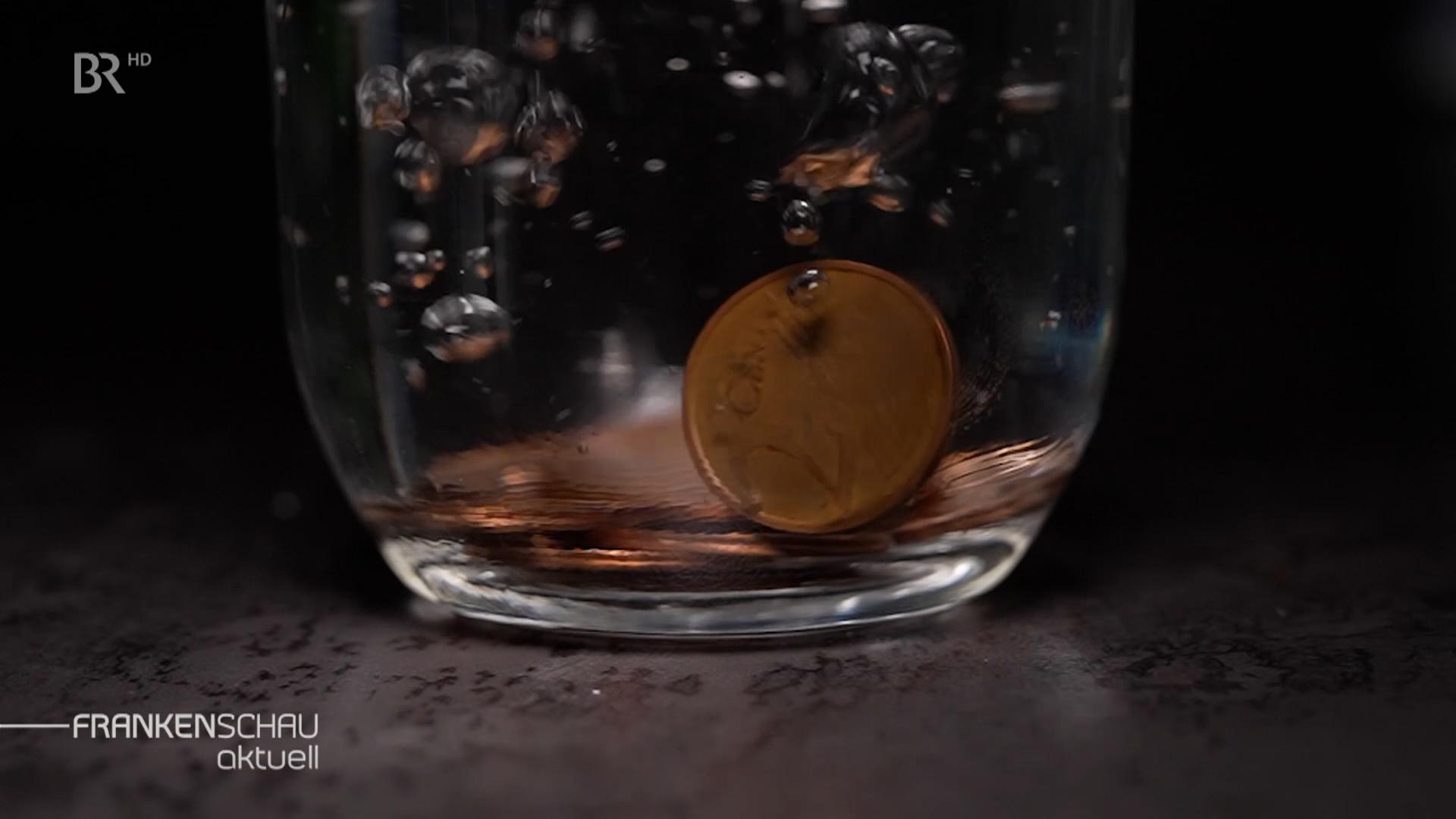 Kupfergeld fällt in Wasserglas.
