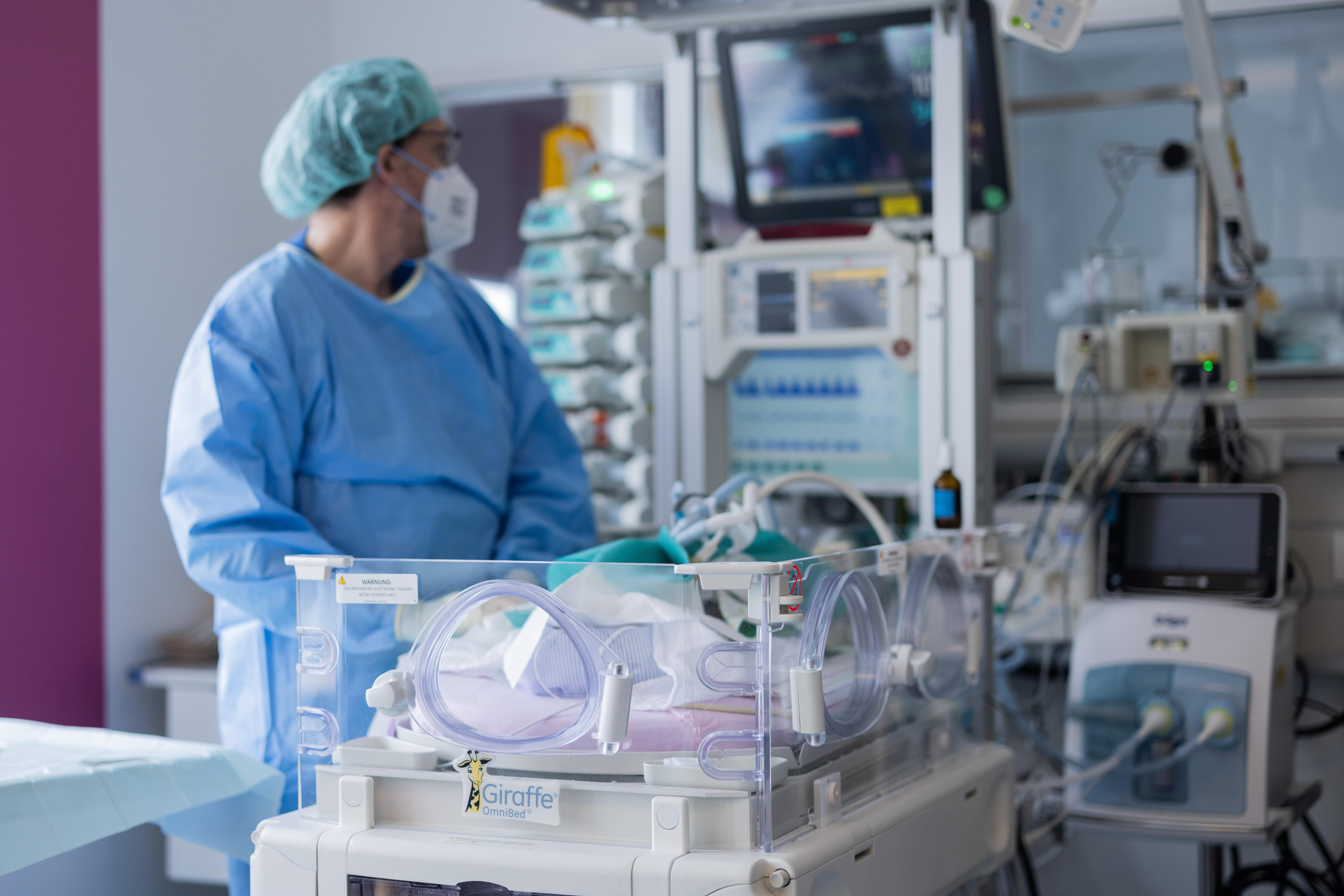Ein Arzt steht in Schutzkleidung und mit Maske in einer Intensivstation und schaut auf einen Monitor.