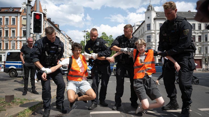Polizeibeamte heben zwei Klimaaktivisten der Gruppe «Letzte Generation» von einer Straße. 