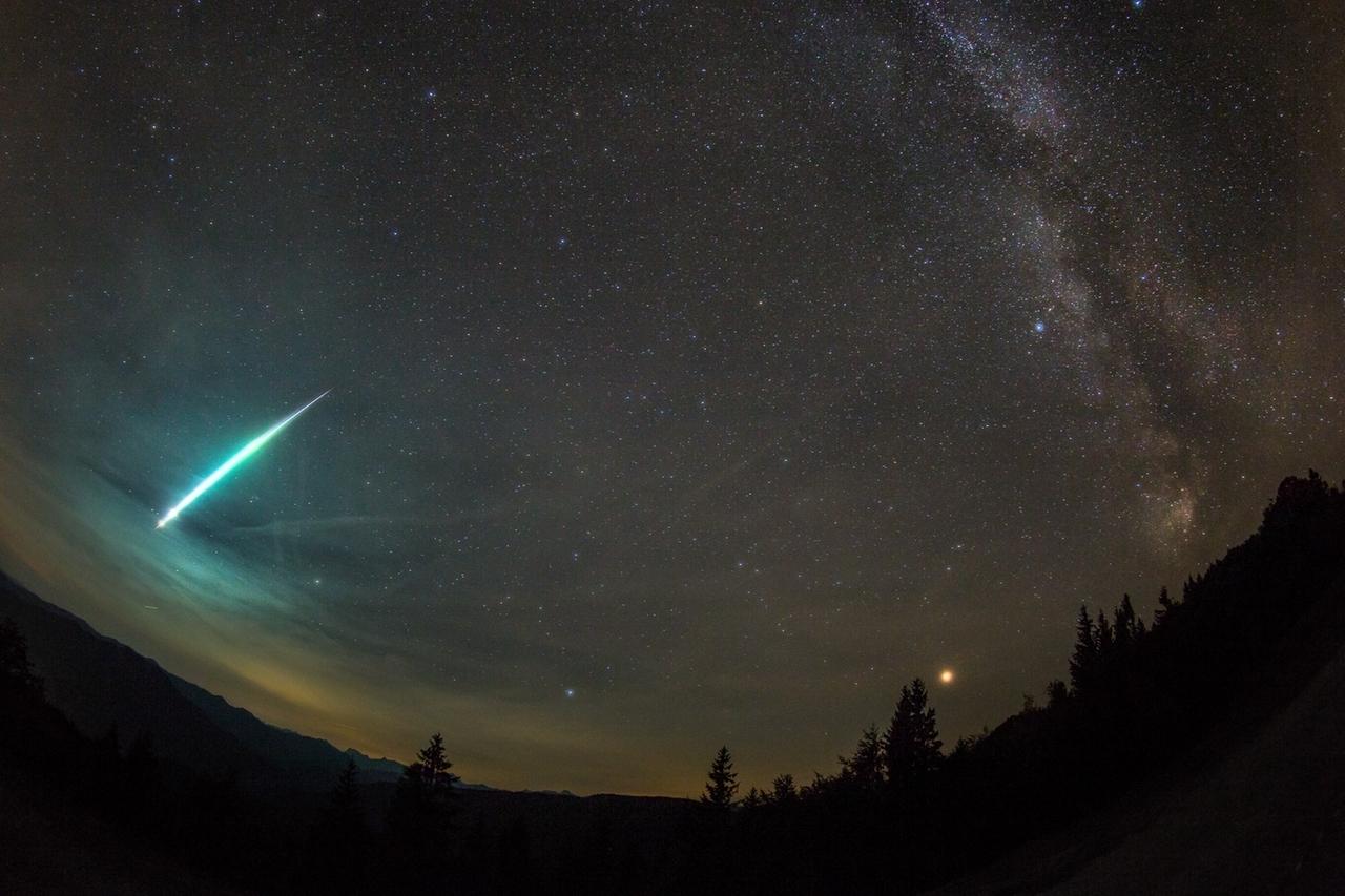 Nicht alle Sternschnuppen sind winzig klein: Manche Meteorschauer haben sogenannte Boliden im Gepäck. Das sind große Leuchtkugeln, oft mit Schweif. Diese Aufnahme zeigt einen Boliden vom September 2018, aufgenommen in Österreich. Rechts im Bild ist die Sommermilchstraße zu sehen, daneben leuchtet rot der Planet Mars. 