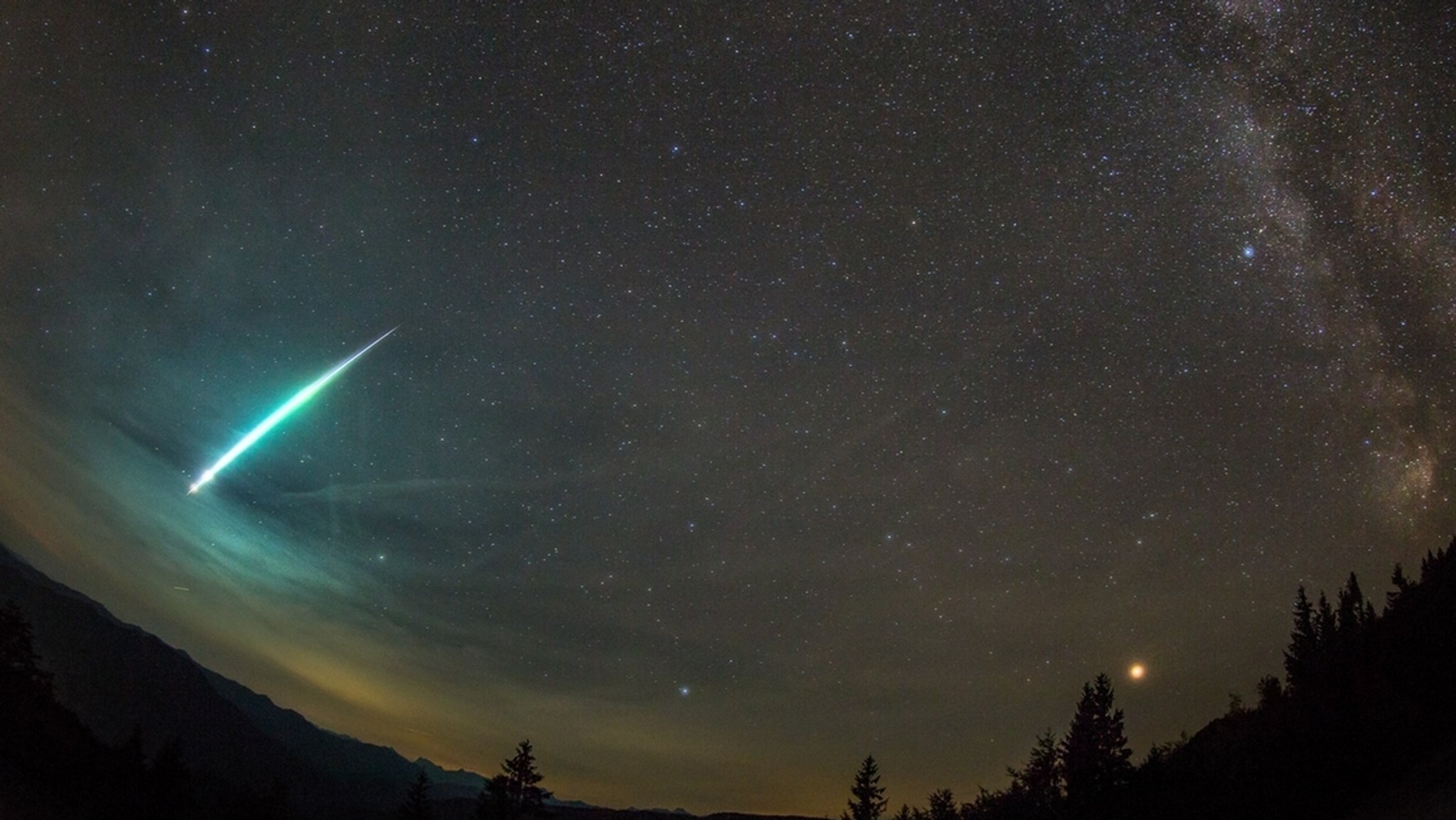 Nicht alle Sternschnuppen sind winzig klein: Manche Meteorschauer haben sogenannte Boliden im Gepäck. Das sind große Leuchtkugeln, oft mit Schweif. Diese Aufnahme zeigt einen Boliden vom September 2018, aufgenommen in Österreich. Rechts im Bild ist die Sommermilchstraße zu sehen, daneben leuchtet rot der Planet Mars. 