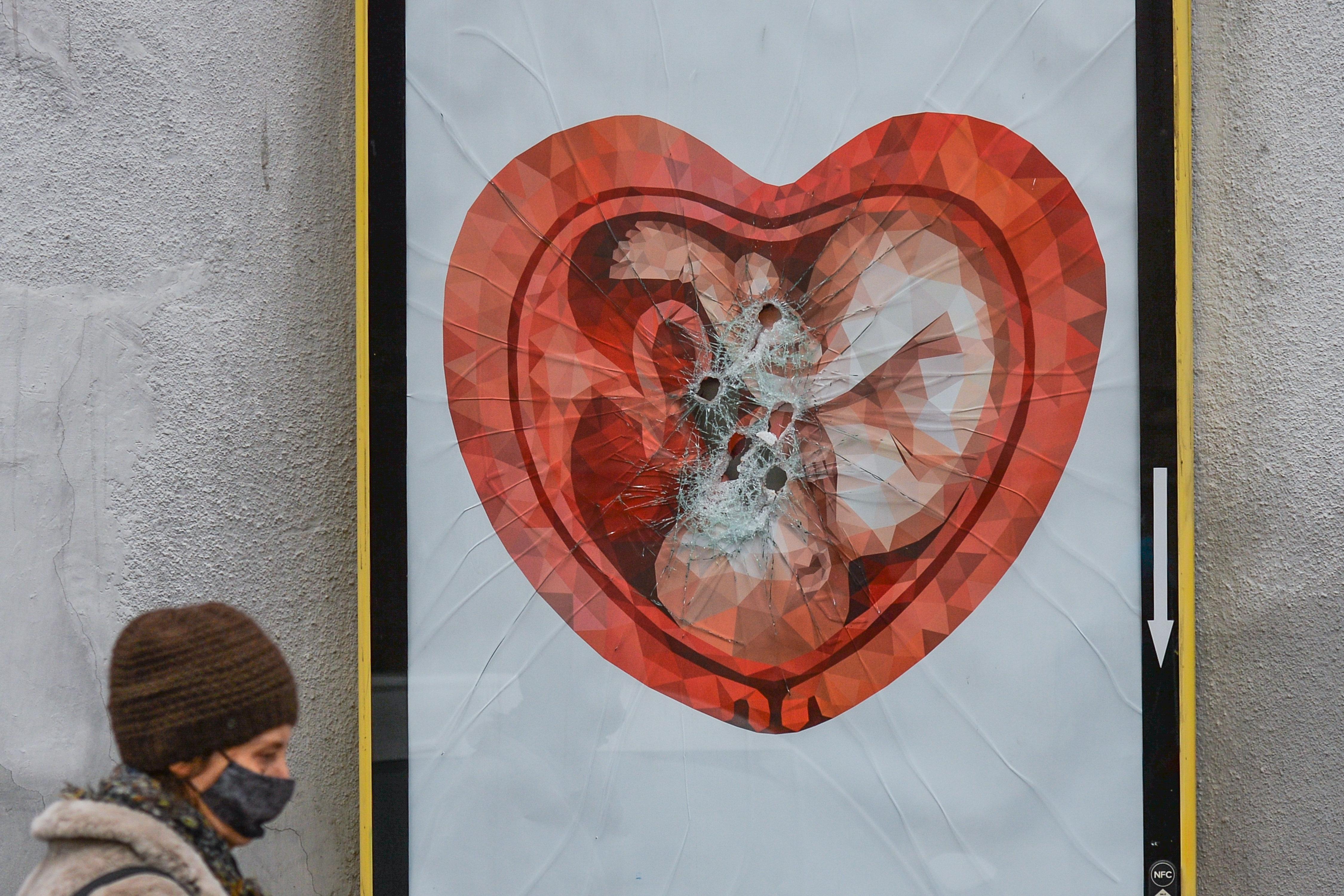 Eine Frau geht an einer zerstörten Werbetafel mit dem Bild eines Fötus in einer herzförmigen Gebärmutter vorbei.