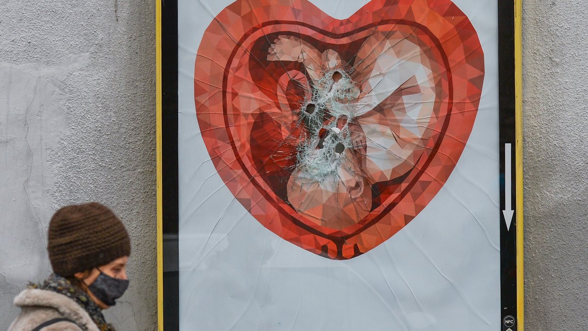Eine Frau geht an einer zerstörten Werbetafel mit dem Bild eines Fötus in einer herzförmigen Gebärmutter vorbei.