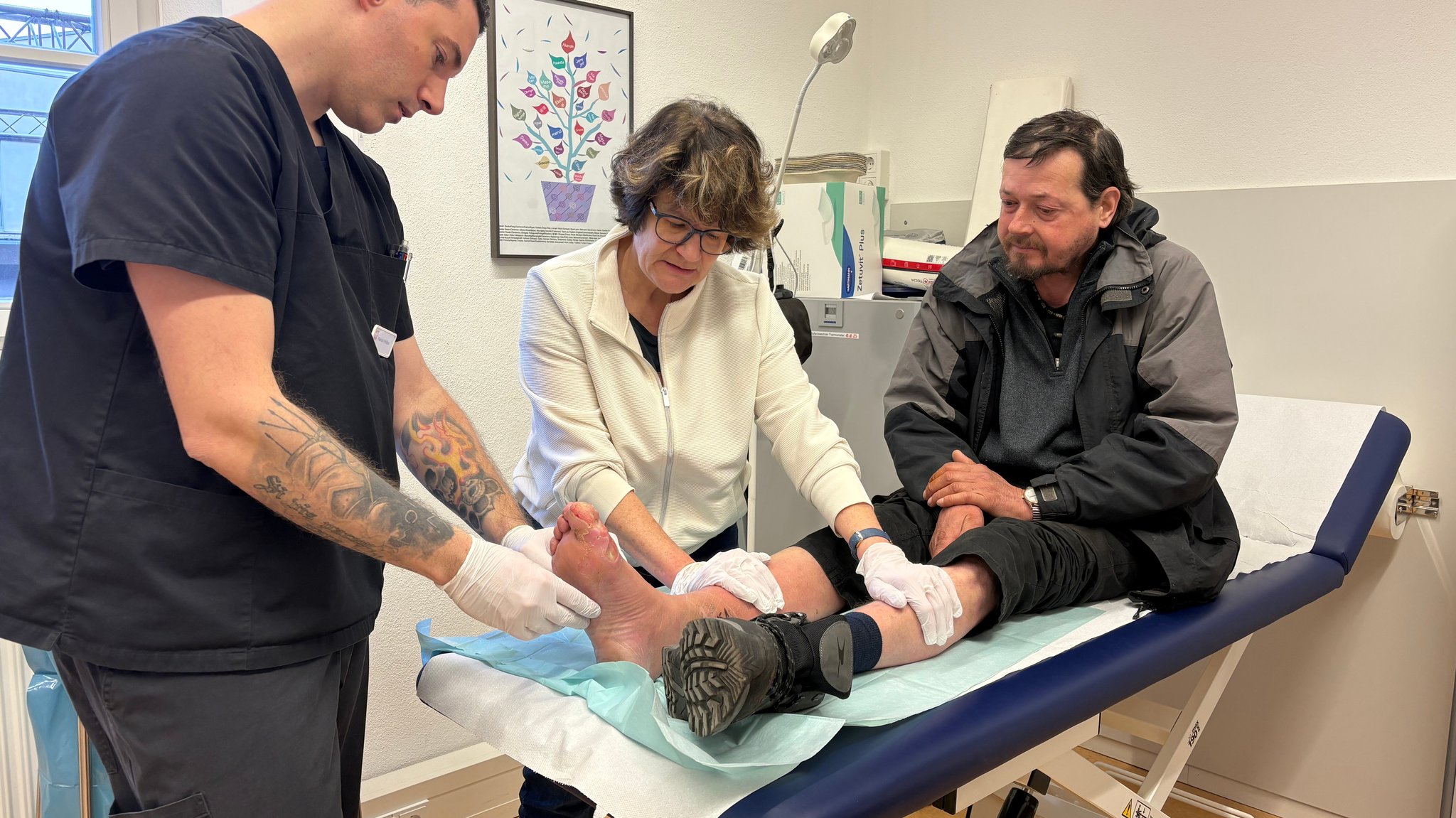 Zwei Menschen der Caritas versorgen den verwundeten Fuß eines Patienten.