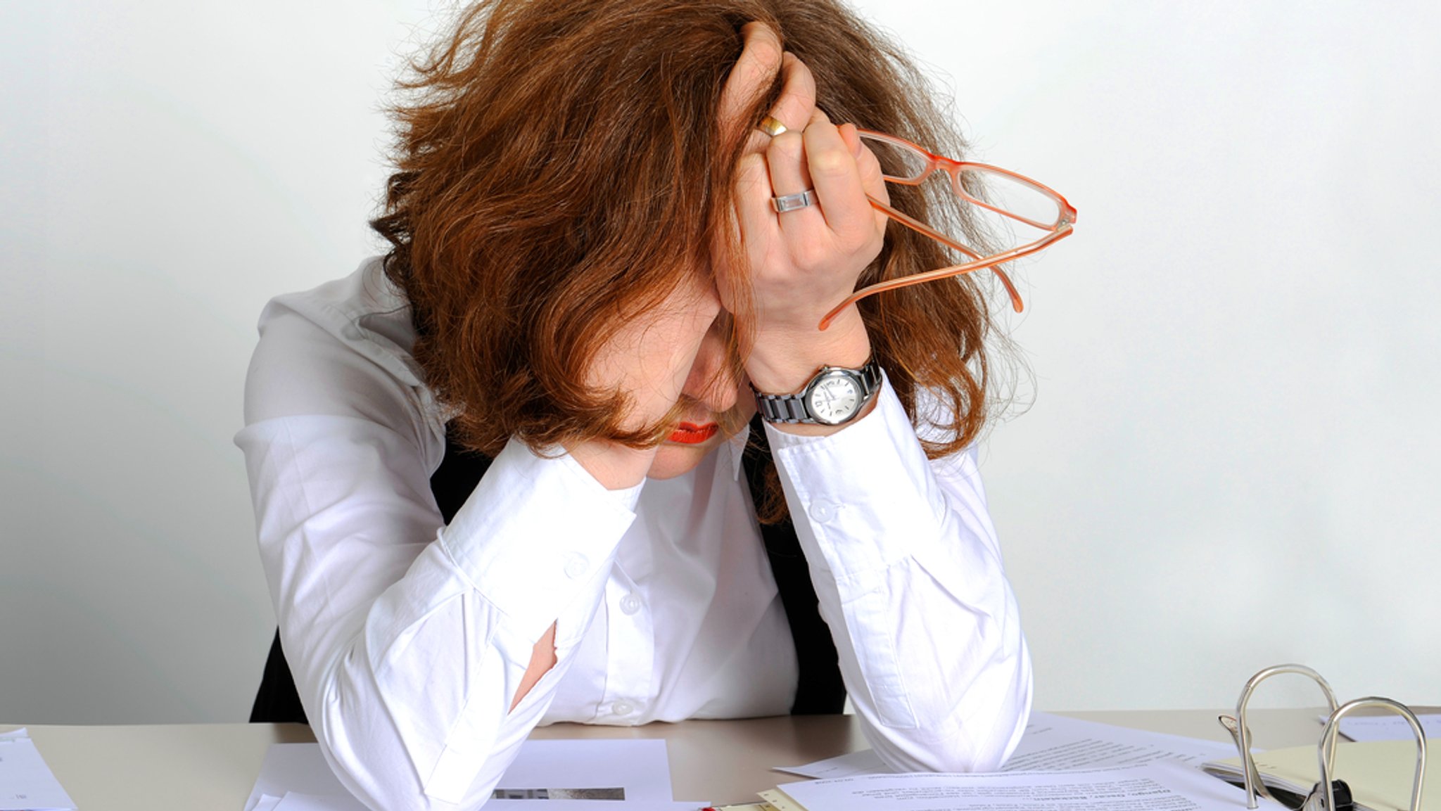 Eine Frau im Büro verbirgt erschöpft das Gesicht in den Händen (Symbolbild)