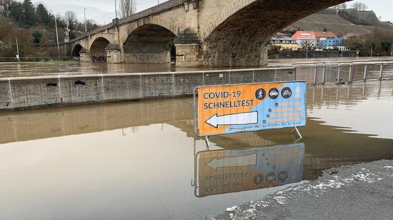 Hochwasser überflutet einen Parkplatz in Würzburg. Ein Schild weist auf ein Corona-Testzentrum hin.