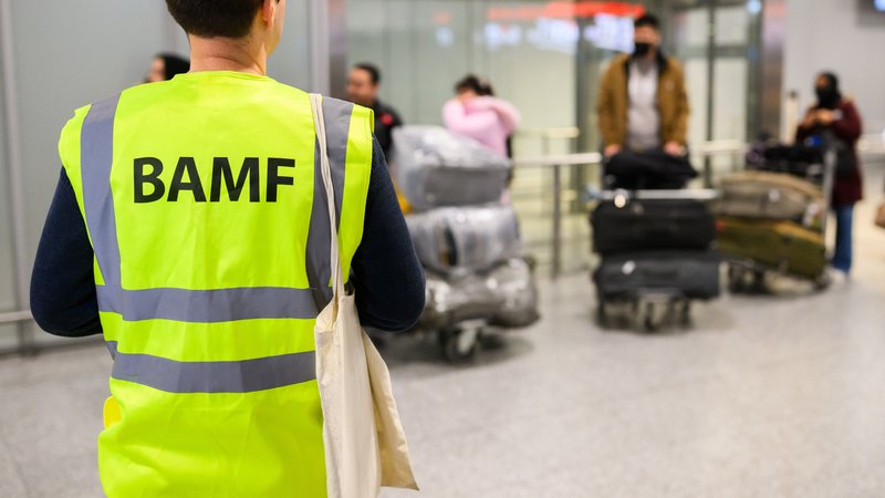 ARCHIV (20.11.2025): Ein Mitarbeiter vom BAMF Bundesamt für Migration und Flüchtlinge steht im Flughafen Hannover vor Afghaninnen und Afghanen aus den Bundesaufnahmeprogrammen. Zum sechsten Mal seit dem Regierungswechsel sind in der pakistanischen Hauptstadt Islamabad Afghanen mit Aufnahmezusage Richtung Deutschland geflogen. | Bild: picture alliance/dpa | Julian Stratenschulte ARCHIV (20.11.2025): Ein Mitarbeiter vom BAMF Bundesamt für Migration und Flüchtlinge steht im Flughafen Hannover vor Afghaninnen und Afghanen aus den Bundesaufnahmeprogrammen. Zum sechsten Mal seit dem Regierungswechsel sind in der pakistanischen Hauptstadt Islamabad Afghanen mit Aufnahmezusage Richtung Deutschland geflogen.