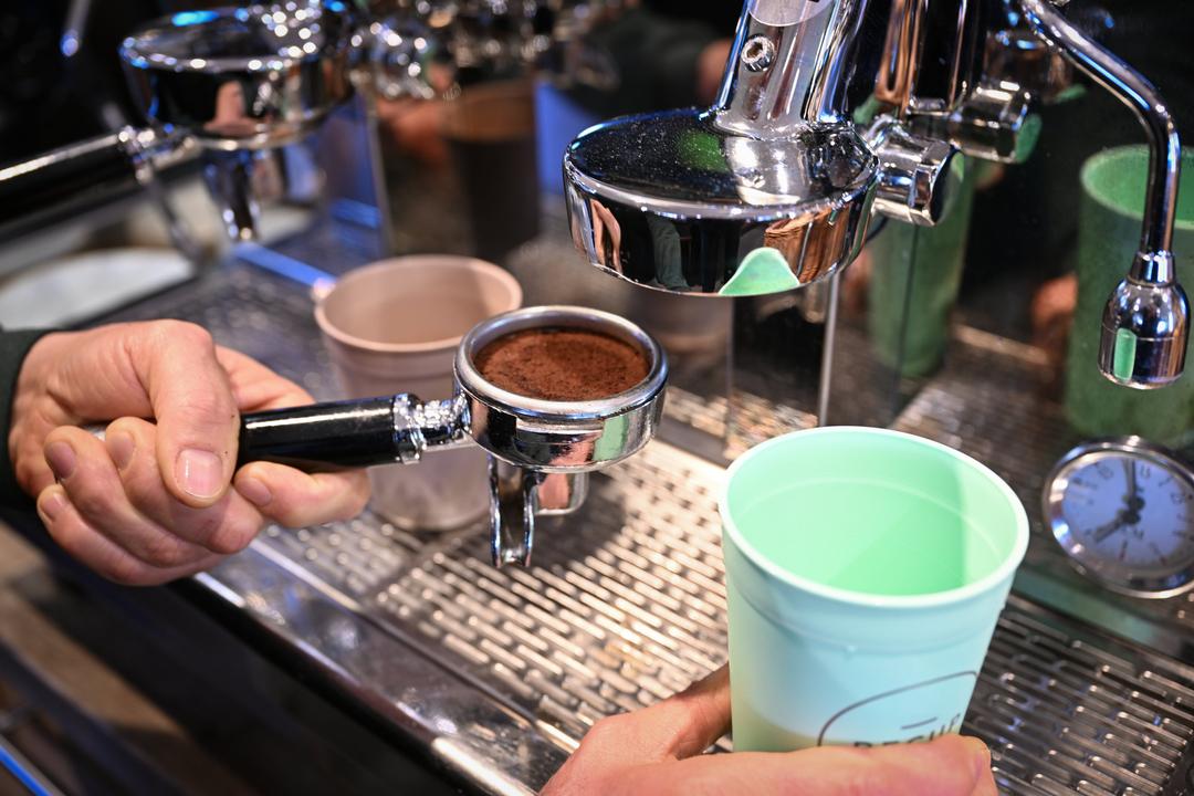 Ein Mitarbeiter eines Ladens bereitet einen Kaffee in einem Mehrwegbecher zu 