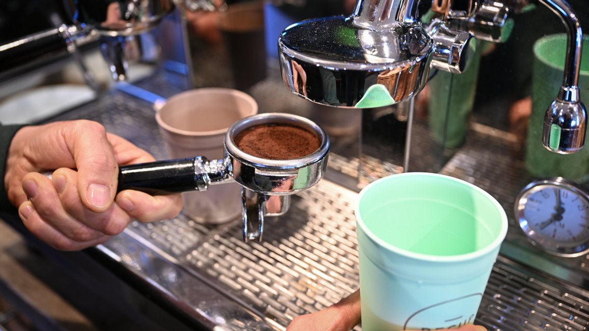 Ein Mitarbeiter eines Ladens bereitet einen Kaffee in einem Mehrwegbecher zu 