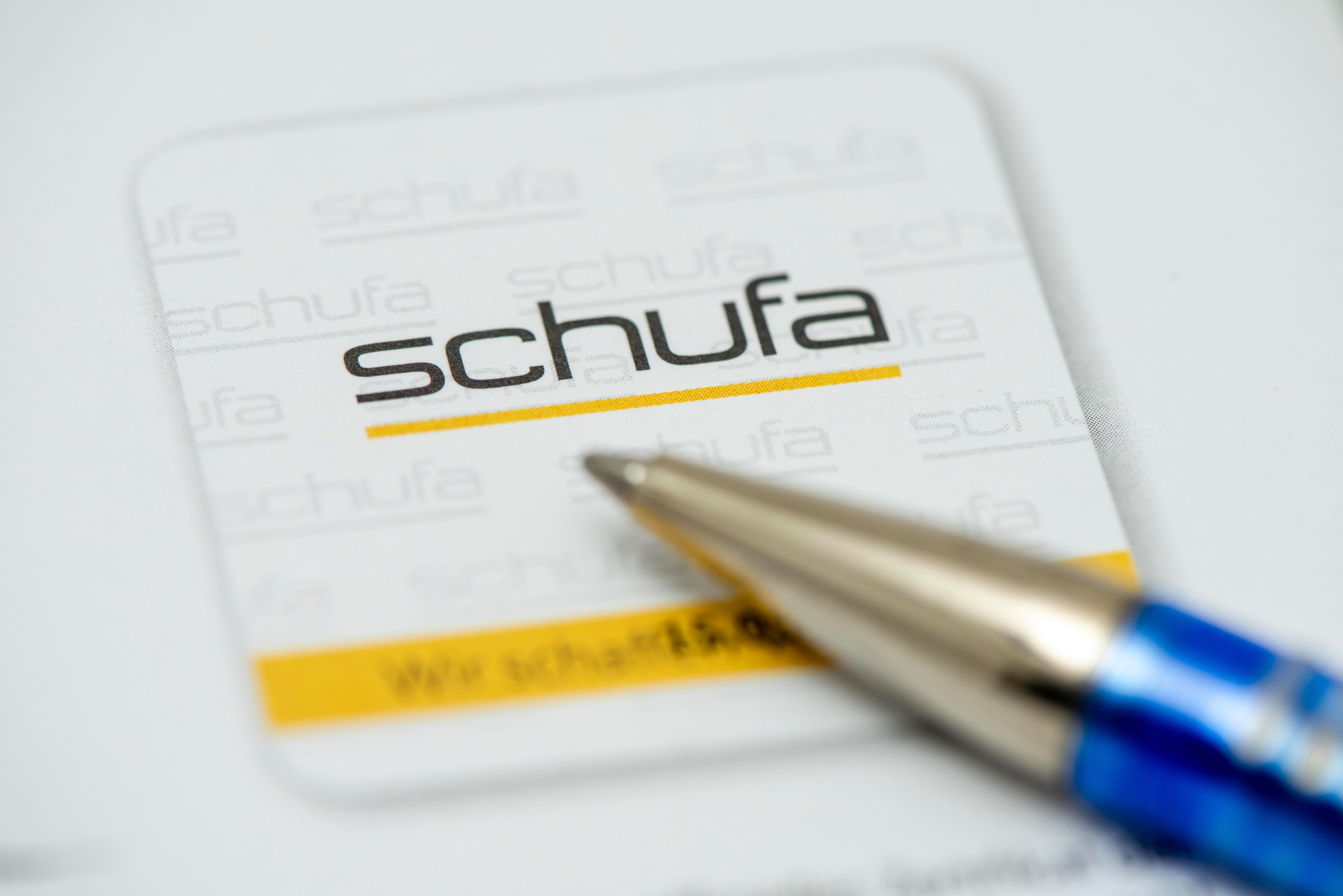 Die Spitze eines Kugelschreibers liegt auf dem Logo der Auskunftei Schufa