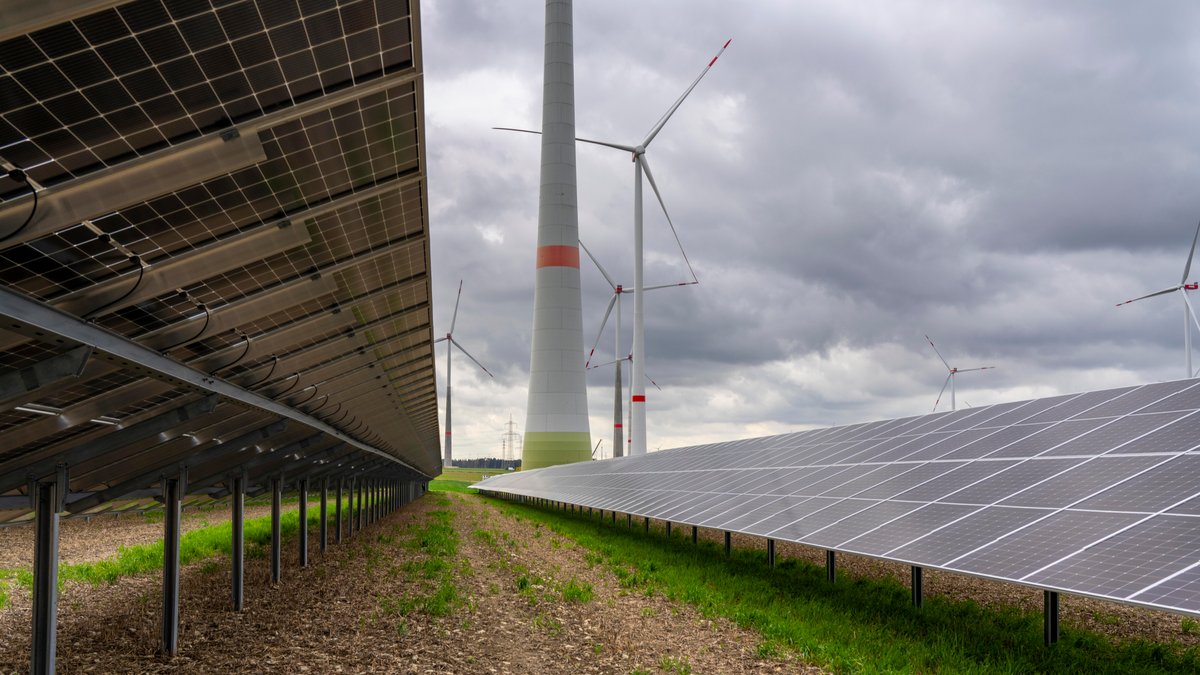 Eine großflächige Photovoltaik-Anlage im Vordergrund, im Hintergrund sieht man mehrere Windräder eines Windparks (Symbolbild)