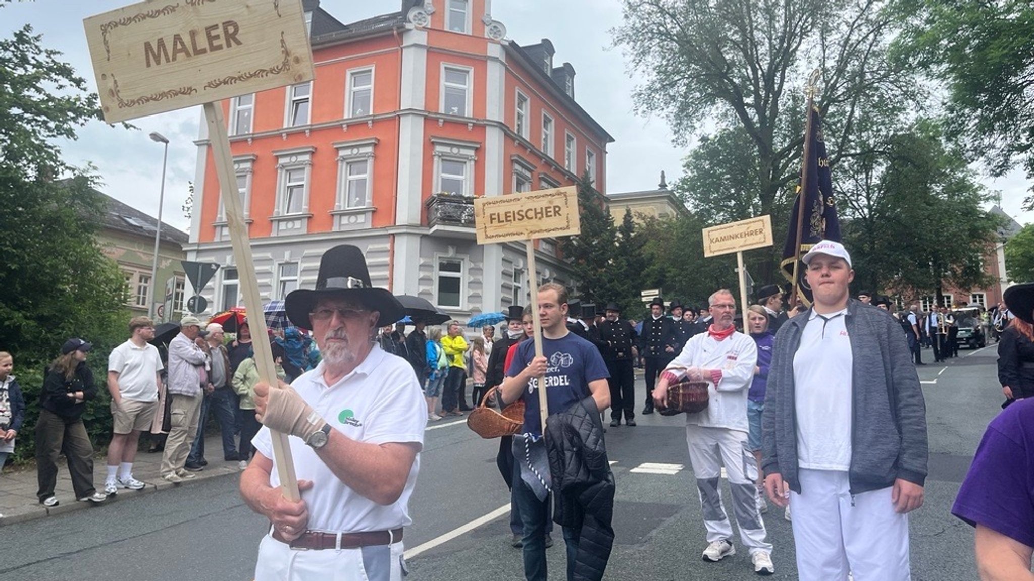 Meister und Gesellen tragen Schilder mit der Aufschrift ihrer jeweiligen Innung.