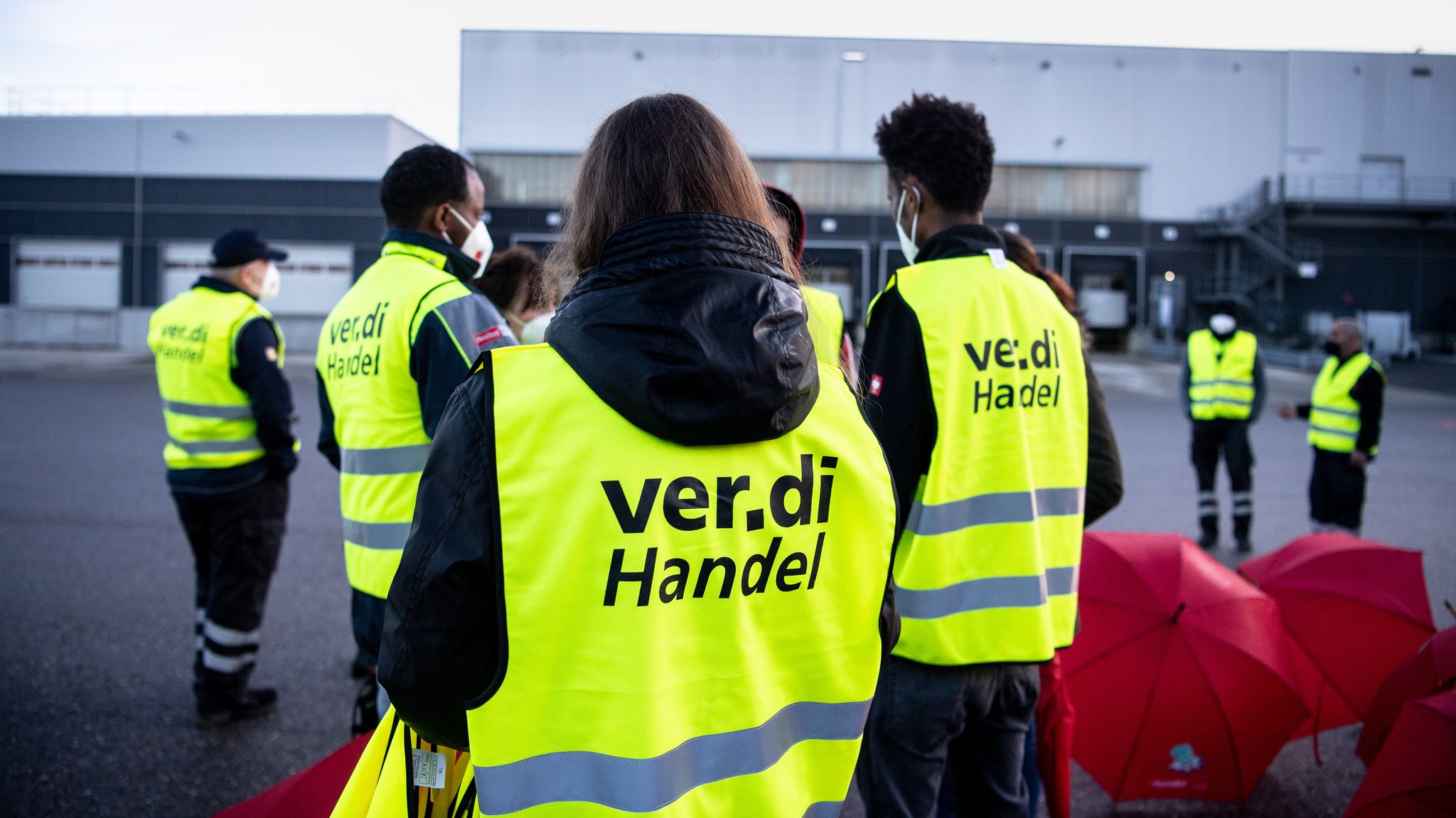 Mitarbeiter eines Lagers stehen bei einem Warnstreik mit Warnwesten mit der Aufschrift „ver.di Handel“ vor einem Lager des Discounters. 