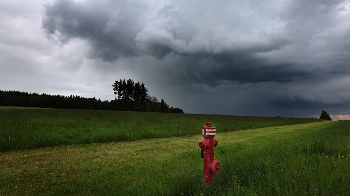 Ein roter Hydrant steht unter dichten Regenwolken auf einer Wiese.