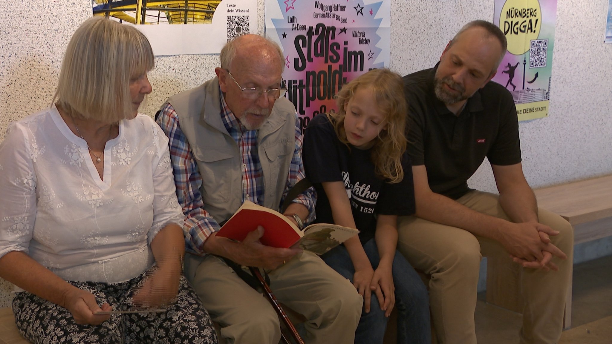 Eine Familie sitzt auf einer Bank und liest in einem Jubiläumsheft.
