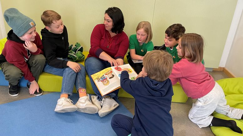 Eine Pädagogin mit einem Buch ist umringt von Grundschulkindern.  | Bild:BR/Frank Strerath