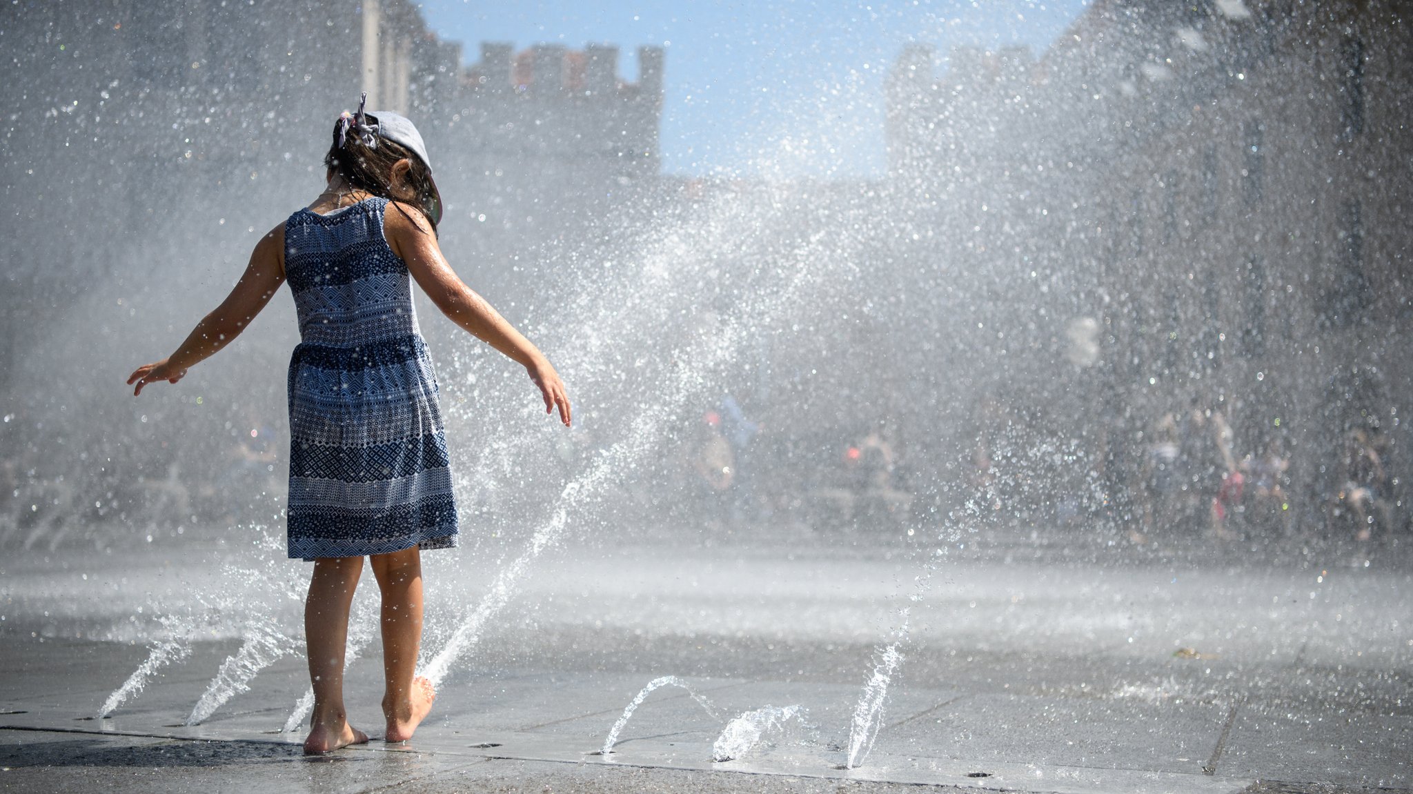 (Symbolbild) Ein Mädchen spielt am Springbrunnen am Stachus in München mit den Wasserfontänen.
