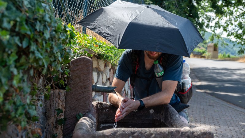 Mann mit Schirm hält Hände unter Wasser eines Brunnens | Bild: picture alliance/dpa | Harald Tittel Mann mit Schirm hält Hände unter Wasser eines Brunnens