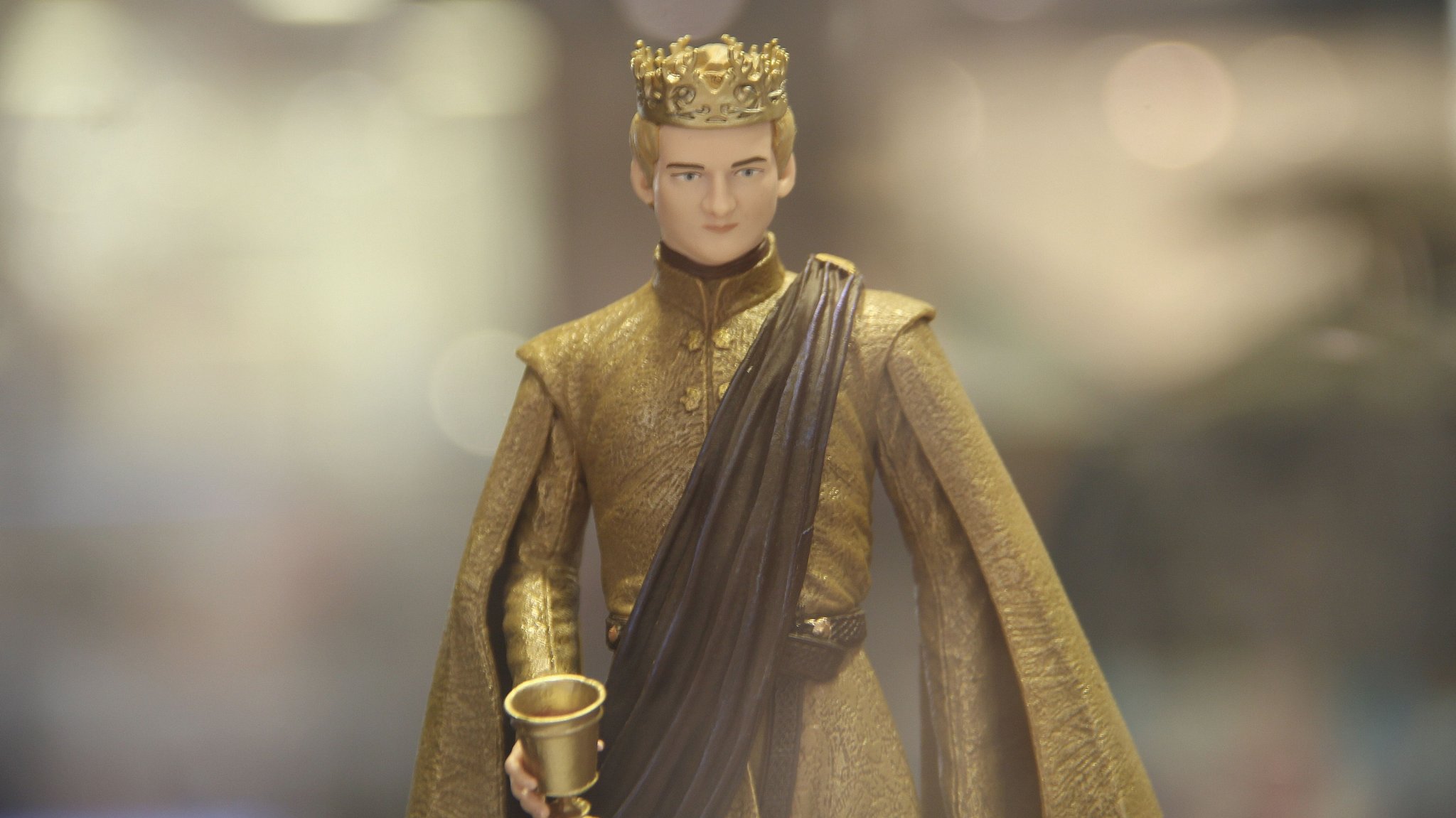 Eine Spielfigur von Joffrey Baratheon aus "Game of Thrones" mit Krone auf dem Kopf und goldenem Becher in der Hand vor unscharfem Hintergrund