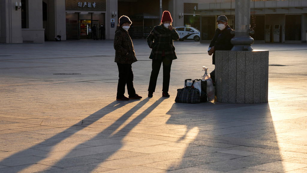 Peking, China: Maskierte Anwohner unterhalten sich auf einem leeren Platz vor dem Bahnhof.