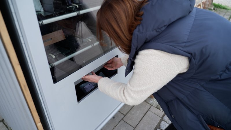 BR-Korrespondentin Katharina Reichart, wie sie ein Paket aus der Klappe des Secret-Pack-Automaten in Niederrieden nimmt.