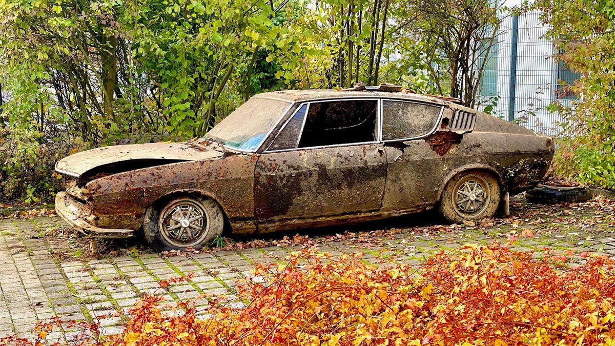 Das aus dem Pfreimdstausee gezogene Autowrack auf einem Parkplatz. Im Vordergrund buntes Herbstlaub.
