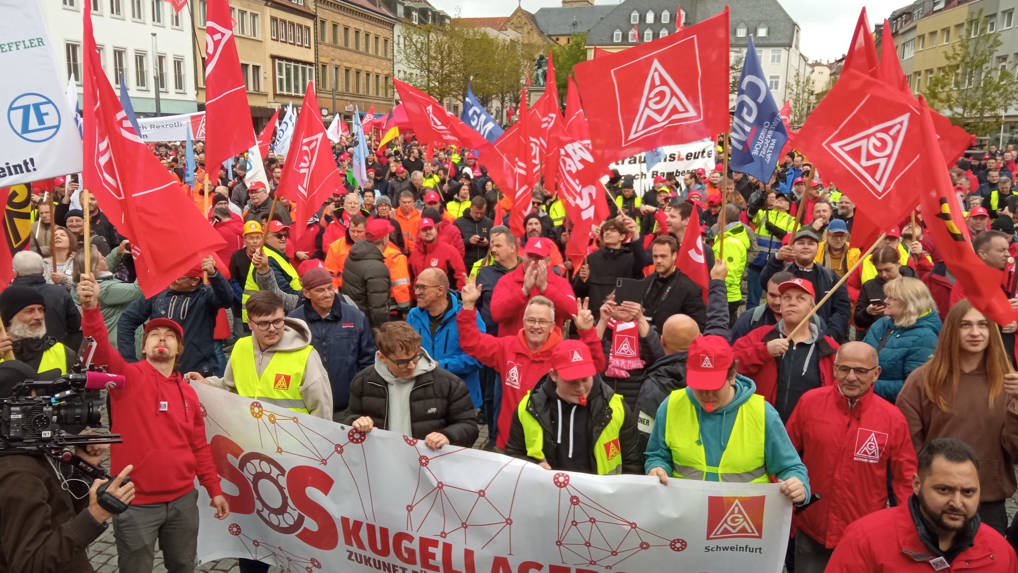 Demonstrantinnen und Demonstranten schwenken Fahnen bei der Groß-Demo der IG-Metall in Schweinfurt.