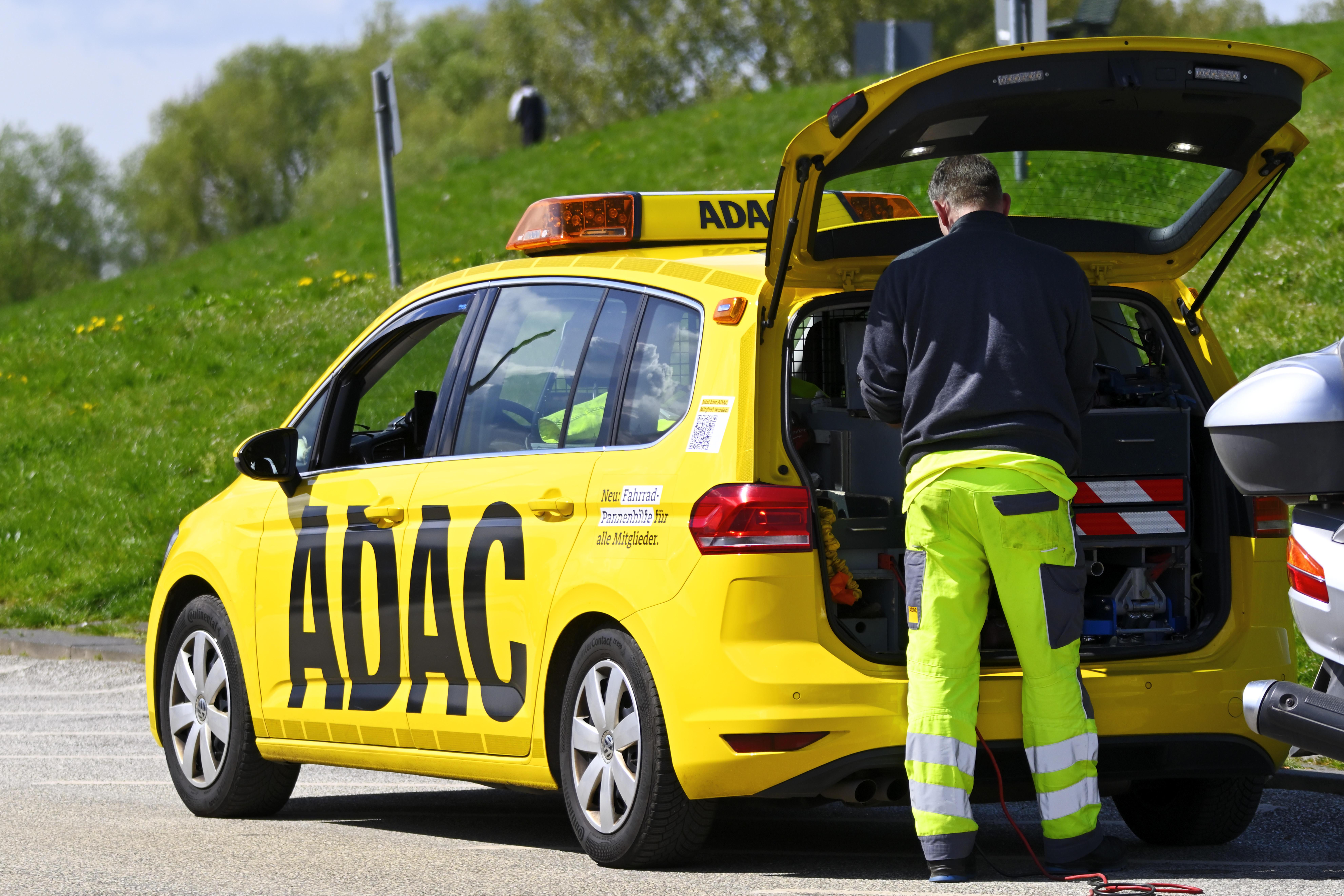 Ein ADAC-Mitarbeiter in neun-warngelber Arbeitshose steht am geöffneten Kofferraum seines gelben ADAC-Einsatzfahrzeugs. (Symbolbild)