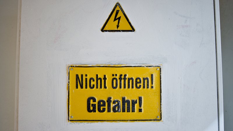 Ein Hinweis "Nicht öffnen! Gefahr!" ist an einem Stromkasten unterhalb einer Warnung vor elektrischem Strom zu sehen (Symbolbild).