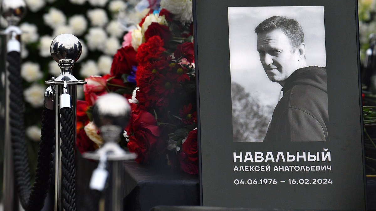 Vor roten Nelken steht ein eingerahmtes Foto von Nawalny mit seinen Lebensdaten